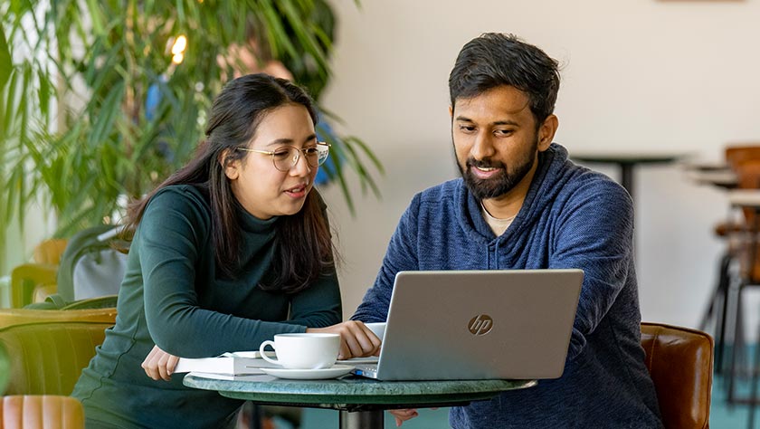 Male and female student sat at a coffee table having a conversation around a laptop.