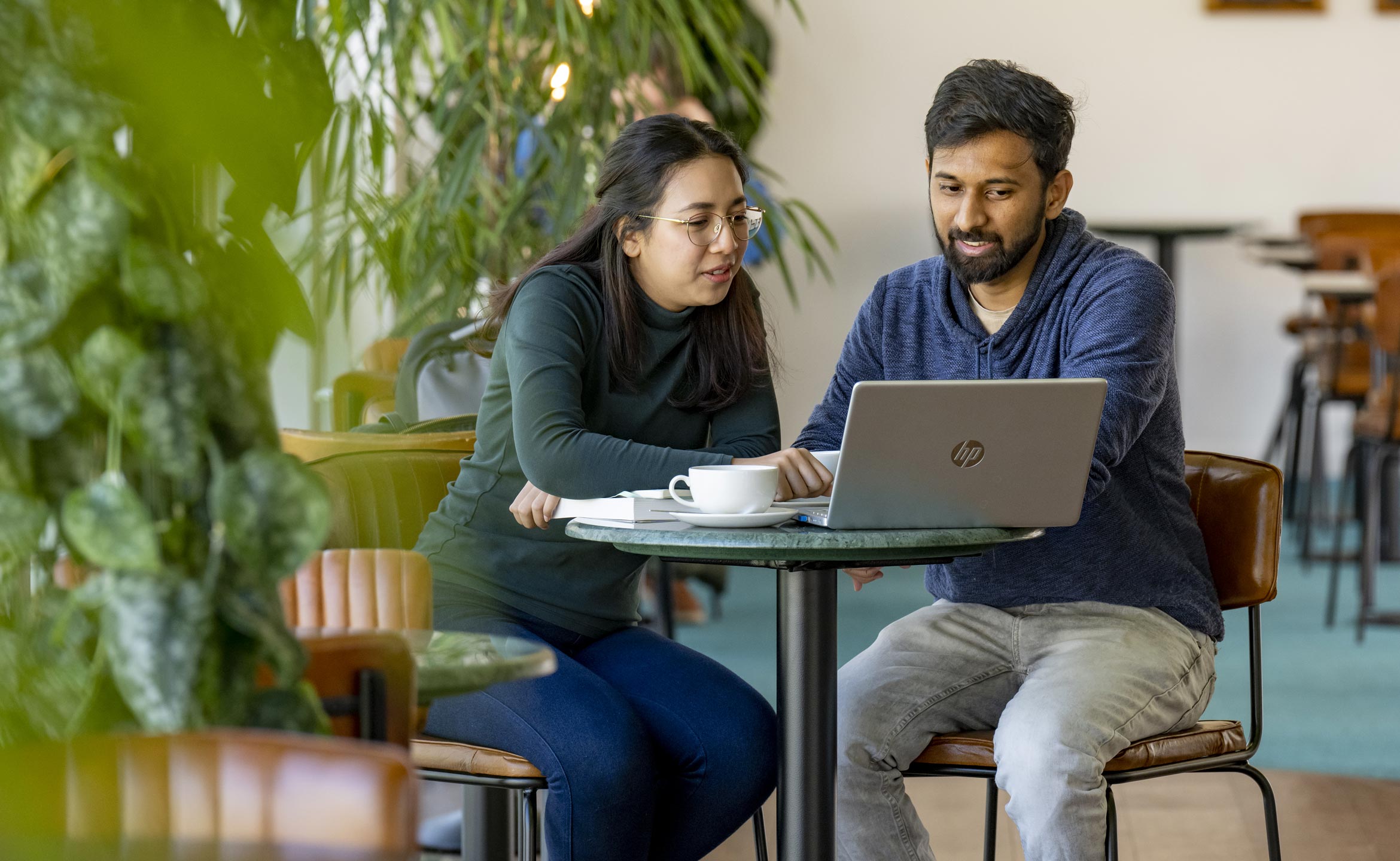 Male and female student sat at a coffee table having a conversation around a laptop.
