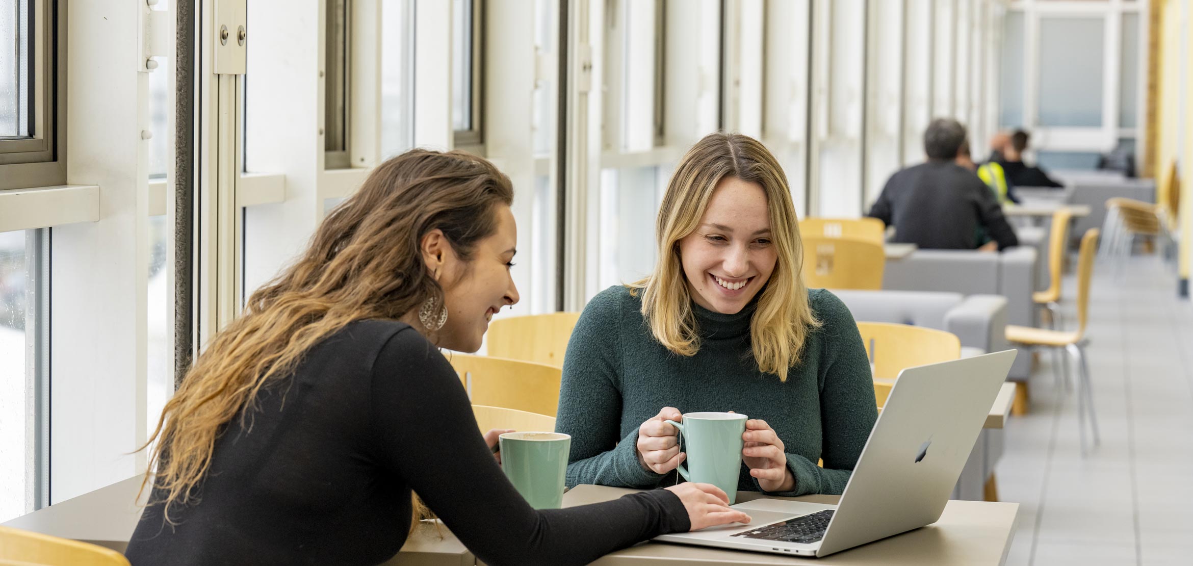 Two students sat opposite each other with laptops in front of them, having a discussion. Both of them are smiling.